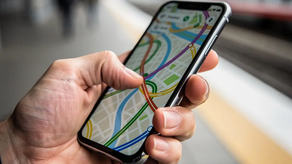 Main tenant un smartphone montrant une carte de trajets alternatifs sur un quai de gare